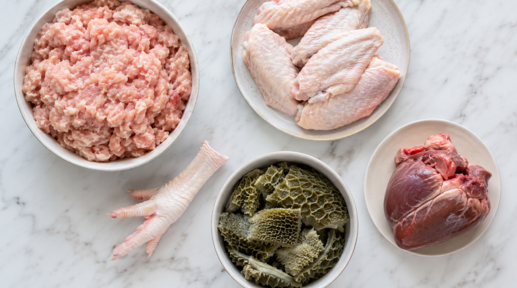 Sourcing raw dog food UK — fresh chicken mince, chicken wings, beef tripe and organ portions laid out on a marble surface